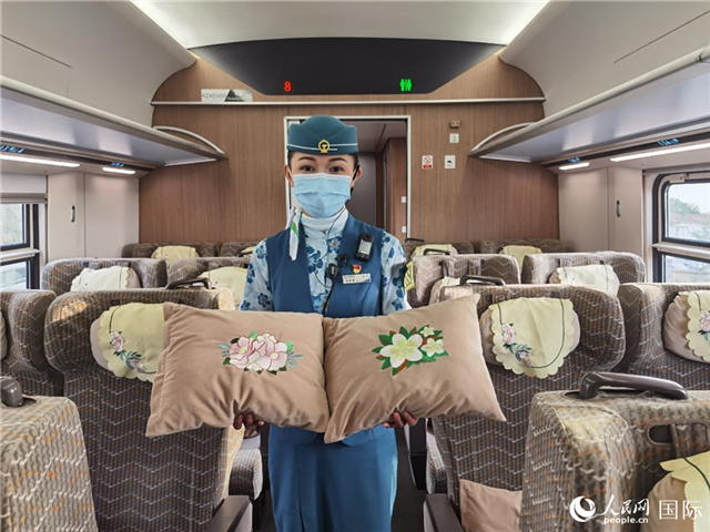 趙瑩靜展示中老鐵路國(guó)際旅客列車?yán)飵в兄袊?guó)牡丹花和老撾占巴花刺繡圖案的靠墊。人民網(wǎng)記者 杜明明攝