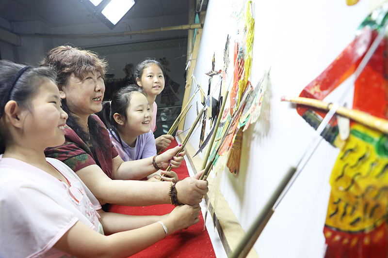 皮影藝人指導(dǎo)小朋友表演皮影戲。